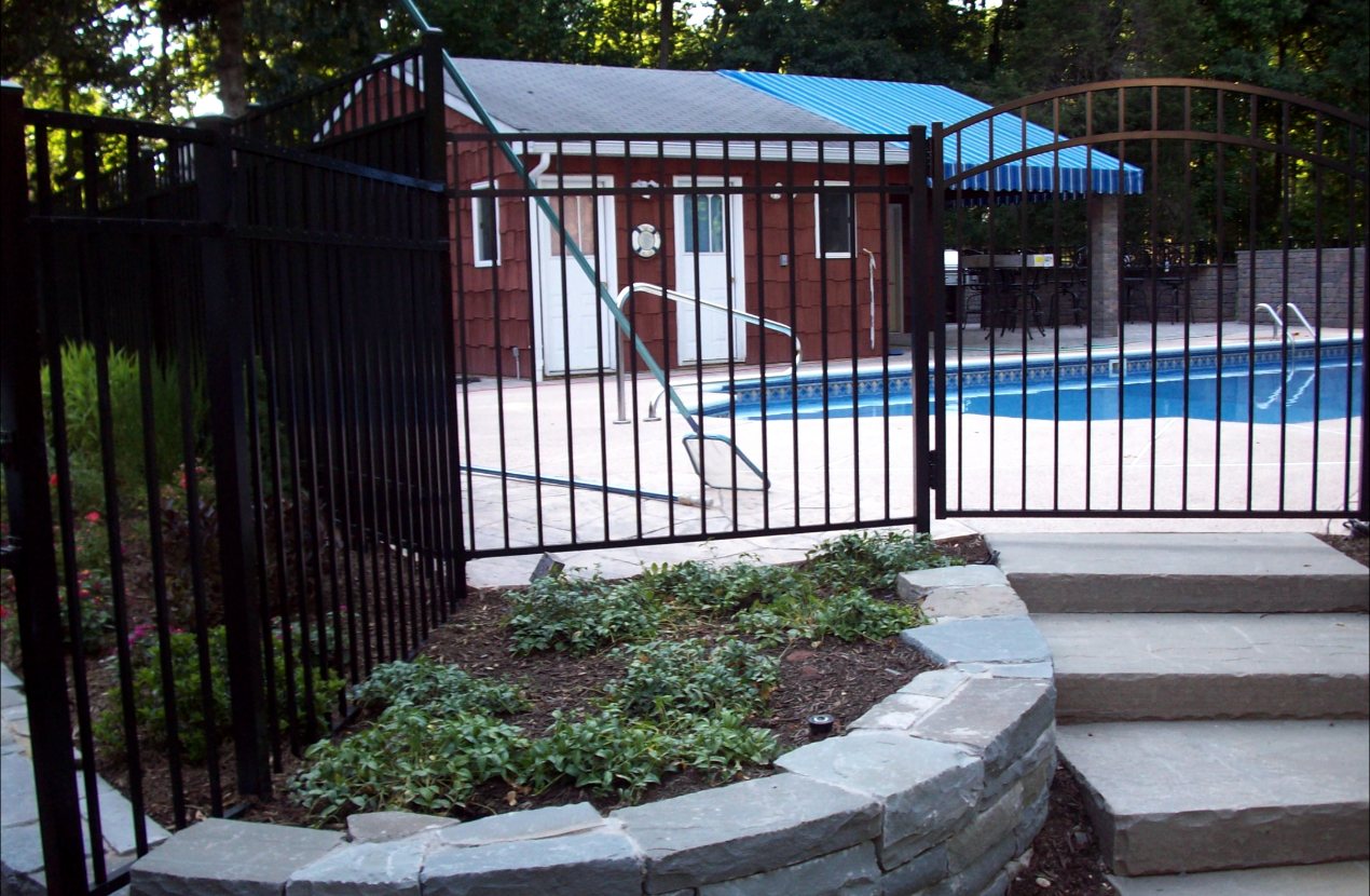 Black aluminum pool fence with an arched walk gate above a curved stone retaining wall